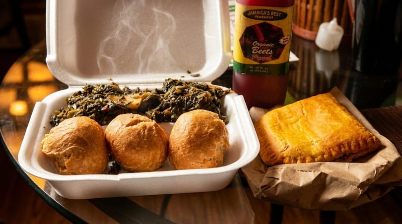 Steaming Jamaican callaloo, three dumplings, and a beef patty with a bottle of beet punch.