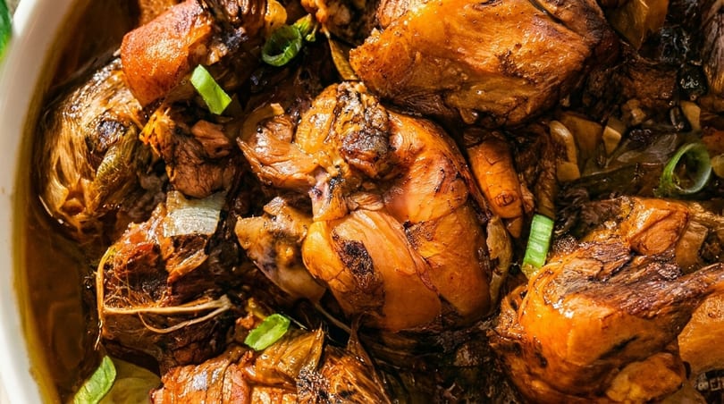 Close-up of savory braised chicken and vegetables in a rich, dark sauce, garnished with green onions.